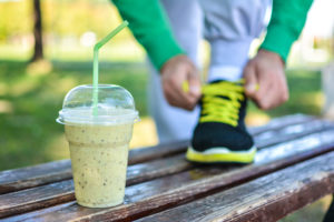 Detox smoothie drink and running footwear close up. Man athlete tying sport shoes.